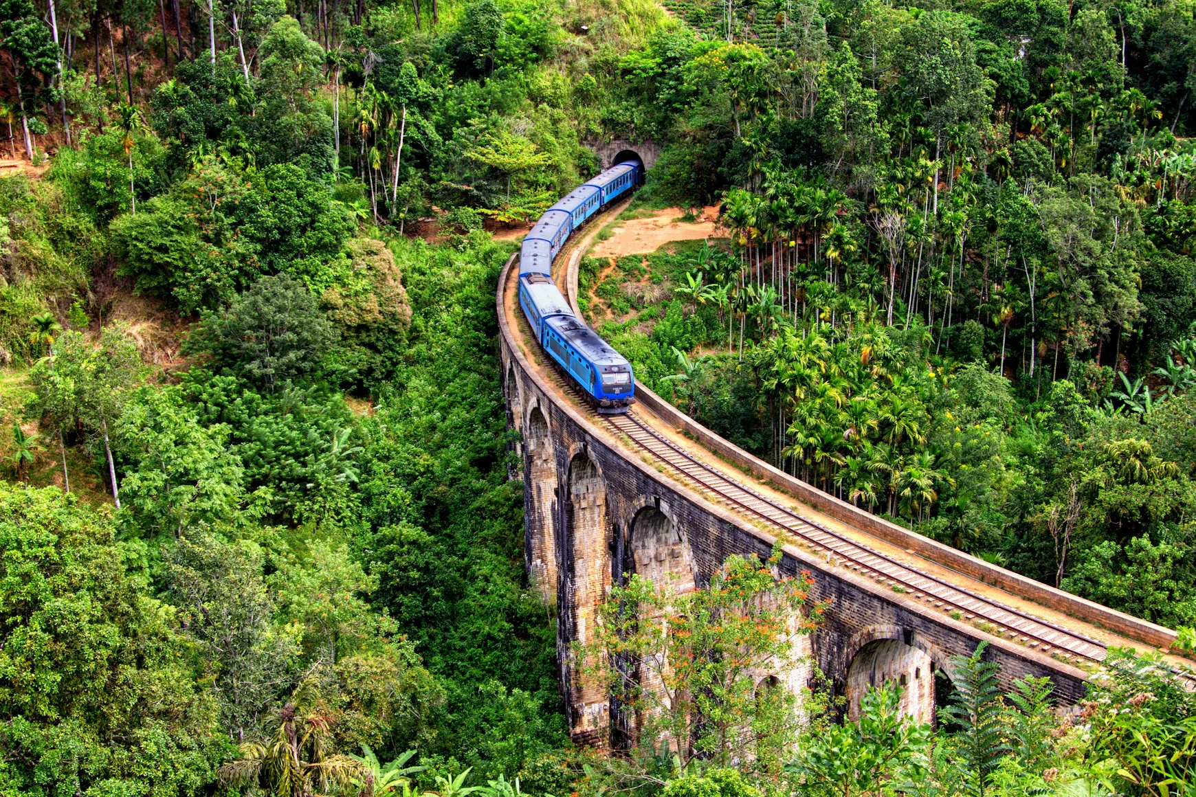 A blue train crossing the Nine Arches Bridge in Sri Lanka's green hills